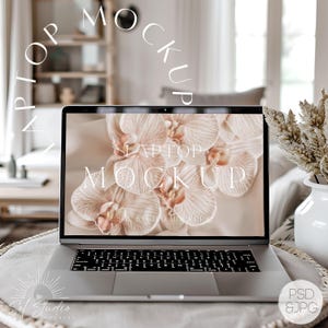 May include: A silver laptop computer with a white background image of orchids on the screen. The text "Laptop Mockup" is displayed on the screen. The laptop is sitting on a light brown surface.