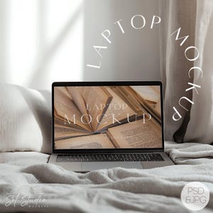 May include: A silver laptop computer with a white screen displaying a mockup of a laptop with the text "Laptop Mockup" and open books. The laptop is on a white bedspread with a white pillow and a beige curtain in the background.