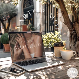 Peut inclure: Un ordinateur portable argenté avec un écran blanc affichant le texte "Laptop Mockup" et une photo d'une femme portant des bijoux. L'ordinateur portable est posé sur une table en bois avec une tasse de café et un téléphone portable.