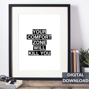 May include: Black and white printable wall art with the text "YOUR COMFORT ZONE WILL KILL YOU". The text is in a bold, sans-serif font and is arranged in a stacked format. The background is white. The image is framed in a black frame and is sitting on a wooden surface.