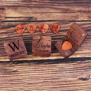 Könnte beinhalten: Ein Set aus sechs Holz-Plektronen mit personalisierten Gravuren. Die Plektren zeigen Namen, Initialen und Daten. Die Plektren werden auf einer Holzoberfläche mit einer kleinen Holzkiste präsentiert.