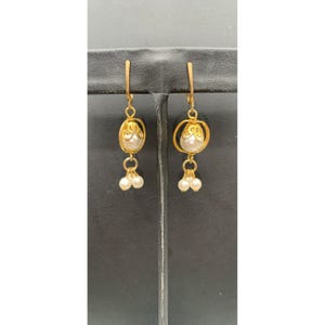 May include: Gold-toned dangle earrings with a pearl and floral design. Each earring features a large, round pearl at the center, surrounded by a gold filigree design. Below the pearl, three smaller pearls dangle, adding movement and elegance.