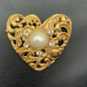 May include: A gold heart-shaped brooch with a pearl and rhinestones.