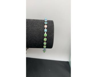 Pulseira de tênis vintage multicolorida com strass que brilham sob luz UV, em tom prateado.