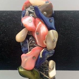 May include: A colorful bracelet featuring a variety of shell-shaped beads in shades of pink, blue, green, and cream. The beads are strung together with silver-colored metal links, creating a unique and eye-catching accessory.