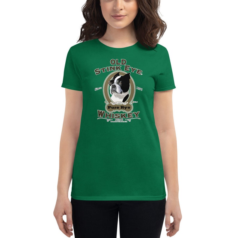 May include: A green women's t-shirt with a vintage-style illustration of a Boston Terrier dog. The illustration is surrounded by a brown oval frame with the text "Old Stink Eye Pure Rye Whiskey" in a brown font.