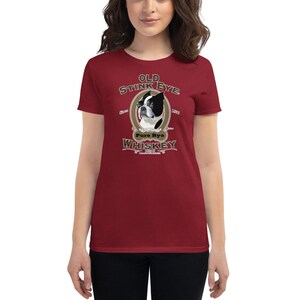 May include: A red women's t-shirt with a vintage-style illustration of a Boston Terrier dog. The illustration is surrounded by a gold oval and the text "Old Stink Eye Pure Rye Whiskey".