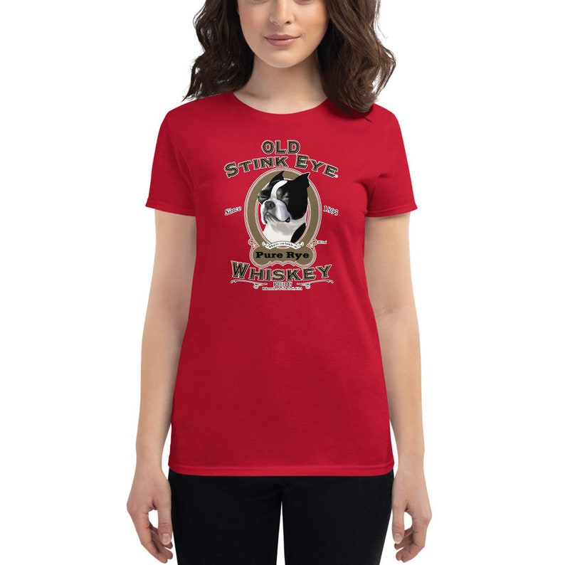May include: Red women's t-shirt with a vintage-style illustration of a Boston Terrier dog. The illustration is surrounded by a gold oval and includes the text "Old Stink Eye Pure Rye Whiskey".