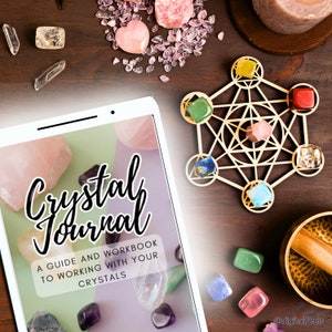 Pode incluir: Uma mesa de madeira exibe um tablet com o texto "Crystal Journal" e "A guide and workbook to working with your crystals." Vários cristais, incluindo quartzo rosa e ametista, circundam um Cubo de Metatron e uma tigela cantora.