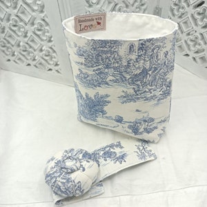 Op de afbeelding: Een witte stoffen opbergmand met een blauw-wit toile-patroon. De mand heeft een label met de tekst "Handmade with Love". Er is ook een bijpassend blauw-wit toile-kussen voor spelden.
