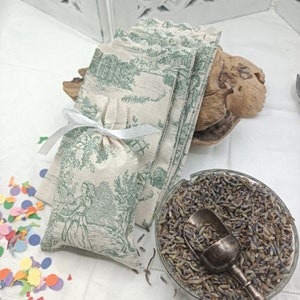Può includere: Un sacchetto di lino bianco con un motivo toile verde e un nastro bianco. Il sacchetto è pieno di fiori di lavanda secchi.