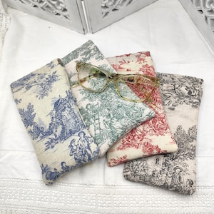 Peut inclure: Quatre étuis à lunettes en tissu à motifs différents. Les étuis sont tous en tissu de couleur claire avec une variété de motifs floraux et de paysages. Un étui a une paire de lunettes claires dessus.