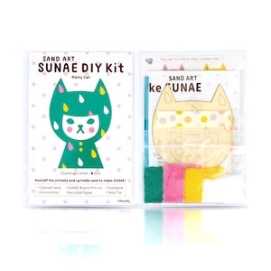 May include: A sand art kit featuring a rainy cat design. The kit includes a wooden cutout of a cat, coloured sand, a toothpick, and a twist tie. The kit is packaged in a clear plastic box with the text "SAND ART SUNAE DIY Kit -Rainy Cat- Challenge Level: ★☆☆ Peel off the stickers and sprinkle sand to make SUNAE! Coloured Sand SUNAE Board (Pre-cut) Toothpick Twist Tie ©Naoshi" printed on the front.