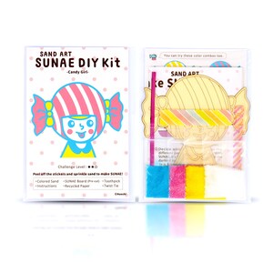 May include: A craft kit for making a sand art picture of a candy girl. The kit includes coloured sand, a pre-cut board, a toothpick, and a twist tie. The packaging is pink and white with the words "SAND ART SUNAE DIY Kit -Candy Girl-  Challenge Level: ★★☆ Peel off the stickers and sprinkle sand to make SUNAE! •Colored Sand •SUNAE Board (Pre-cut) •Toothpick •Instructions •Recycled Paper •Twist Tie ©Naoshi"