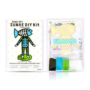 May include: A sand art DIY kit featuring a skeleton fish design. The kit includes coloured sand, a pre-cut board, a toothpick, and a twist tie. The instructions are printed on recycled paper. The kit is labelled "SUNAE DIY Kit -Skeleton Fish-  Challenge Level: ★★"