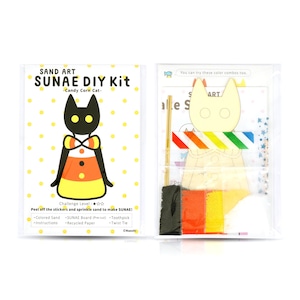 May include: A Sand Art DIY kit with a Candy Corn Cat theme. The kit contains coloured sand, a pre-cut board, a toothpick, instructions, recycled paper, and a twist tie. The packaging displays a finished cat design and the necessary materials.