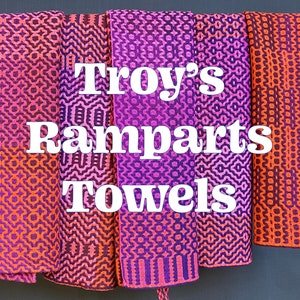 Puede incluir: Cinco toallas coloridas con un patrón geométrico cuelgan de una barra. Las toallas son un degradado de rosa y naranja. El texto "Troy's Ramparts Towels" está superpuesto en las toallas.