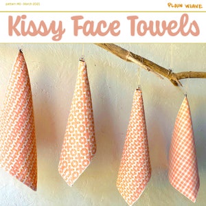 Op de afbeelding: Vier oranje handdoeken met een wit patroon hangen aan een tak. De handdoeken zijn gelabeld met "Kissy Face Towels" en "Plain Weave".