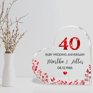 May include: A clear heart-shaped acrylic plaque with the number 40 in red glitter, commemorating a ruby wedding anniversary. The plaque includes the names "Martha & Aitter" and the date 08.12.1985, with red floral accents.