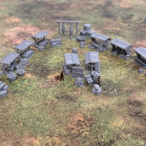 Könnte beinhalten: Miniatur-Marktstände, Fässer und andere mittelalterliche Strukturen in Grau sind auf einer grasbewachsenen Oberfläche angeordnet. Einige kleine Figuren deuten auf eine geschäftige Marktszene hin.