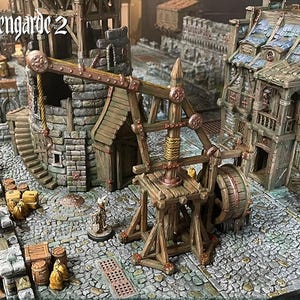May include: A detailed miniature medieval town scene featuring a trebuchet, buildings, and cobblestone streets. The scene is mainly brown, grey, and tan, with the text "hexengarde 2". The trebuchet is constructed from wood and metal.