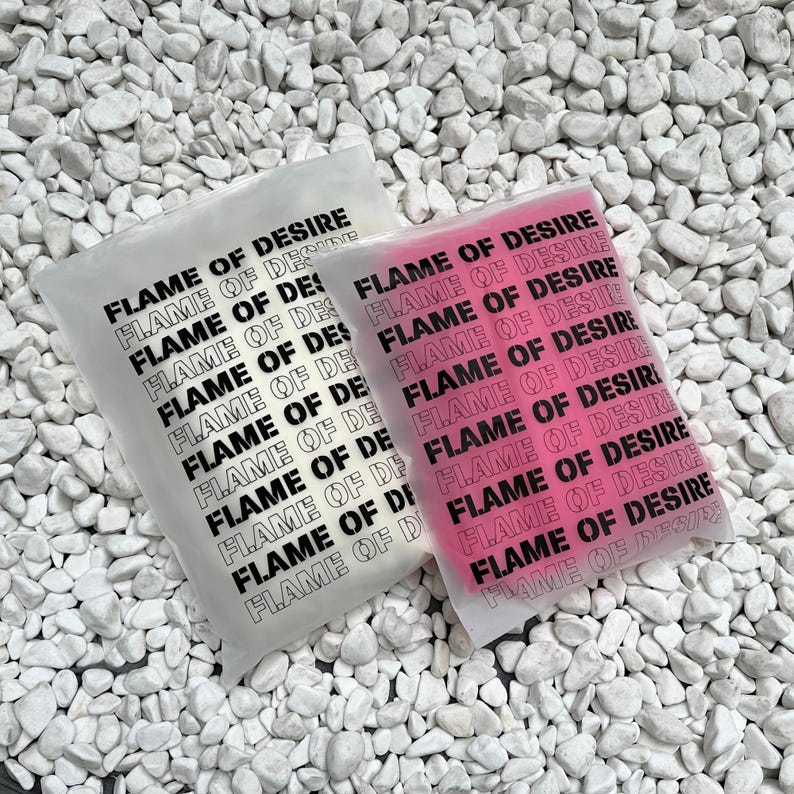 May include: Two clear plastic bags with the text "FLAME OF DESIRE" printed repeatedly in black. One bag is white and the other is pink.