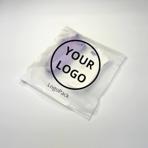 May include: A clear plastic bag with a white and purple fabric inside. The bag has a black circle with the text "YOUR LOGO" and the text "LogoPack" printed on it.