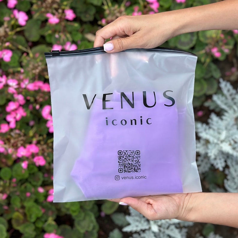 May include: A clear plastic bag with a zipper closure. The bag has a purple lining and the text "VENUS iconic" printed in black. A QR code and the text "@venus.iconic" are also printed on the bag.