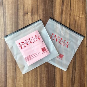 May include: Two clear plastic zippered bags with a red logo that says "зроблено в Харкові INUA" on a light brown wooden surface.