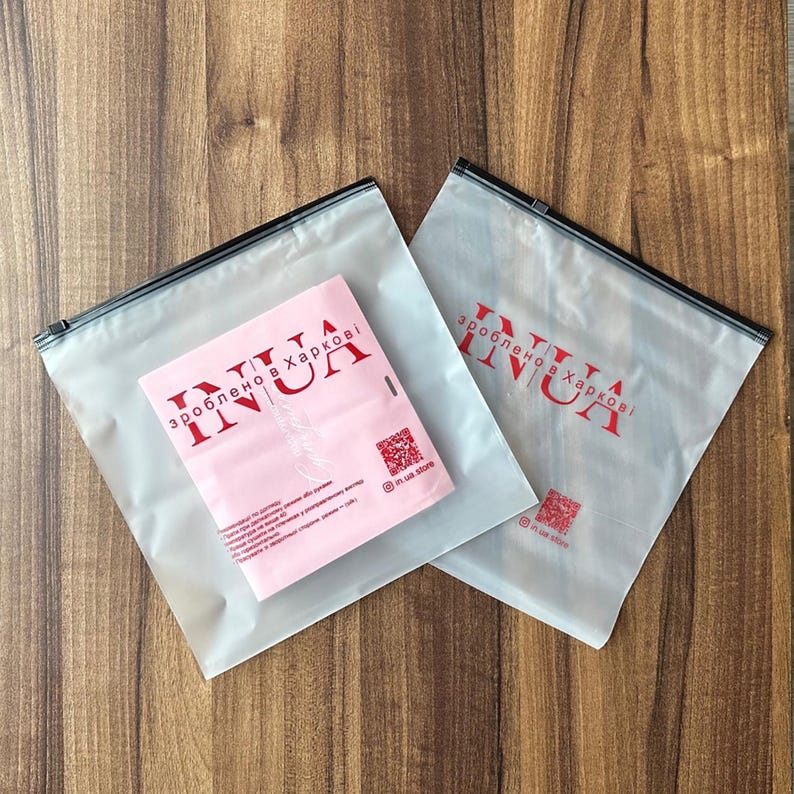 May include: Two clear plastic zippered bags with a red logo that says "зроблено в Харкові INUA" on a light brown wooden surface.