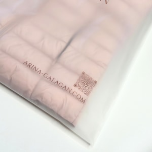 May include: A pink puffer jacket with a white plastic bag. The bag has the text "ARINA-GALAGAN.COM" and a QR code printed on it.