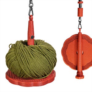 Può includere: Un set di rocchetto e avvolgitore per filato rosso. Il rocchetto ha un bordo decorativo smerlato. L'avvolgitore tiene in mano una matassa di filato verde oliva. Entrambi i pezzi sono sospesi a un cordoncino nero e argento.