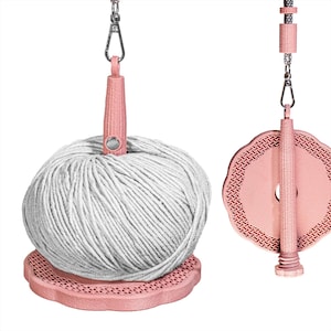 Può includere: Due porta-filo rosa con chiusure in metallo color argento. Uno supporta una grande palla di filo bianco, appoggiata su una base rosa smerlata. L'altro ha un disco rosa decorativo con un bordo a motivi.