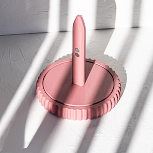 Può includere: Un dispenser di sapone in ceramica rosa per il piano di lavoro con una base rotonda e una pompa cilindrica alta. Il dispenser ha una base testurizzata e rigata.