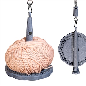 Può includere: Un rocchetto grigio con una palla di filato color pesca. Il rocchetto ha una base decorativa e un palo centrale con una clip per appenderlo. Il filato è ordinatamente avvolto, pronto per progetti di maglia o uncinetto.