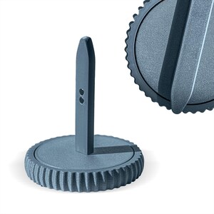 Può includere: Un portarotolo di carta grigio in stile industriale, con una base rotonda e scanalata e un montante verticale con due piccoli fori. È visibile anche la parte superiore del supporto, con un bordo scanalato e una maniglia curva.