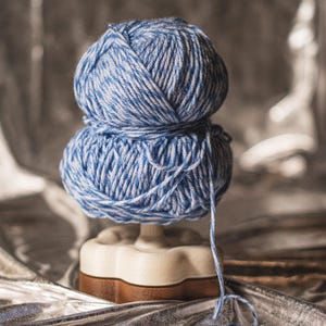 Può includere: Due gomitoli di lana blu e bianca impilati su un porta-lana bianco. La lana è avvolta attorno al supporto ed è pronta per essere utilizzata per la maglia o l'uncinetto.
