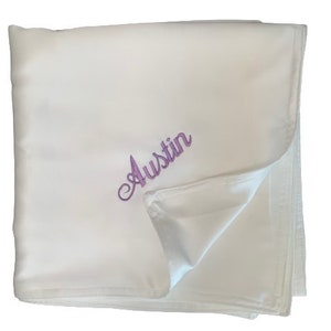 May include: White baby blanket with the name "Austin" embroidered in purple.