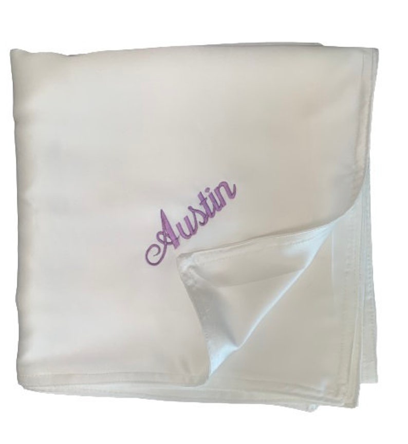 May include: White baby blanket with the name "Austin" embroidered in purple.