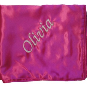 Peut inclure: Une taie d'oreiller en satin rose avec le nom Olivia brodé en blanc.
