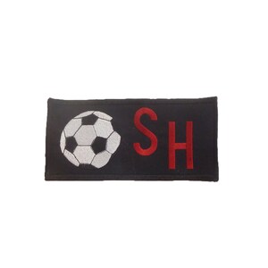 May include: Black fabric patch with a white soccer ball and the red letters "SH" embroidered on it.