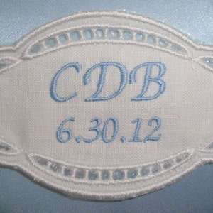 May include: White embroidered oval-shaped fabric label with blue stitching. The label says "CDB 6.30.12".