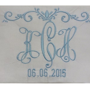 May include: A white fabric with a light blue embroidered monogram of the letters "KCH" in a cursive script. The monogram is topped with a decorative flourish and the date "06.06.2015" is embroidered below.