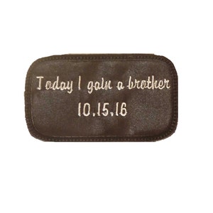 May include: Brown rectangular patch with white embroidered text that reads "Today I gain a brother 10.15.16".