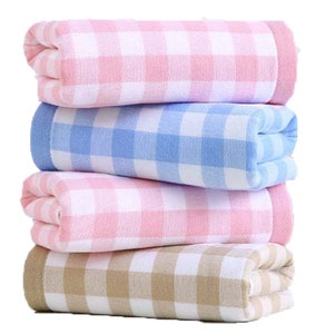 Op de afbeelding: Vier gevouwen katoenen handdoeken met een geruit patroon. De handdoeken zijn roze, blauw en beige.