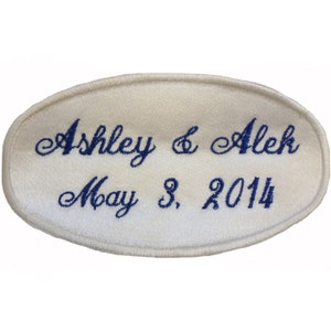May include: White oval satin patch with blue embroidered text that reads "Ashley & Alek May 3, 2014".