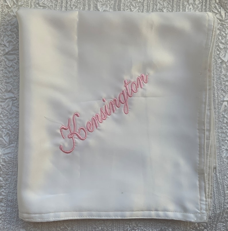May include: White satin baby blanket with pink embroidery that says "Kensington".