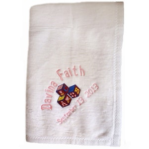 May include: White baby blanket with pink embroidery that reads "Davina Faith September 13, 2013" and a colorful embroidered image of alphabet blocks.