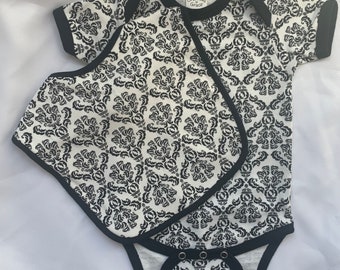 ダマスク柄の黒と白のモチーフとお揃いのよだれかけが付いた魅力的な幼児用ボディスーツ