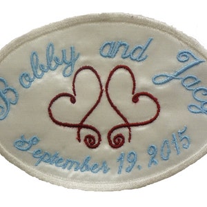 May include: White oval satin patch with blue embroidery that reads "Bobby and Lacy September 19, 2015". Two intertwined red hearts are embroidered in the center.